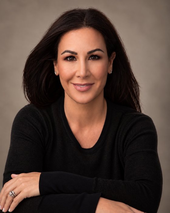 Portrait of Elyse Messing, smiling, arms folded, in a black sweater.